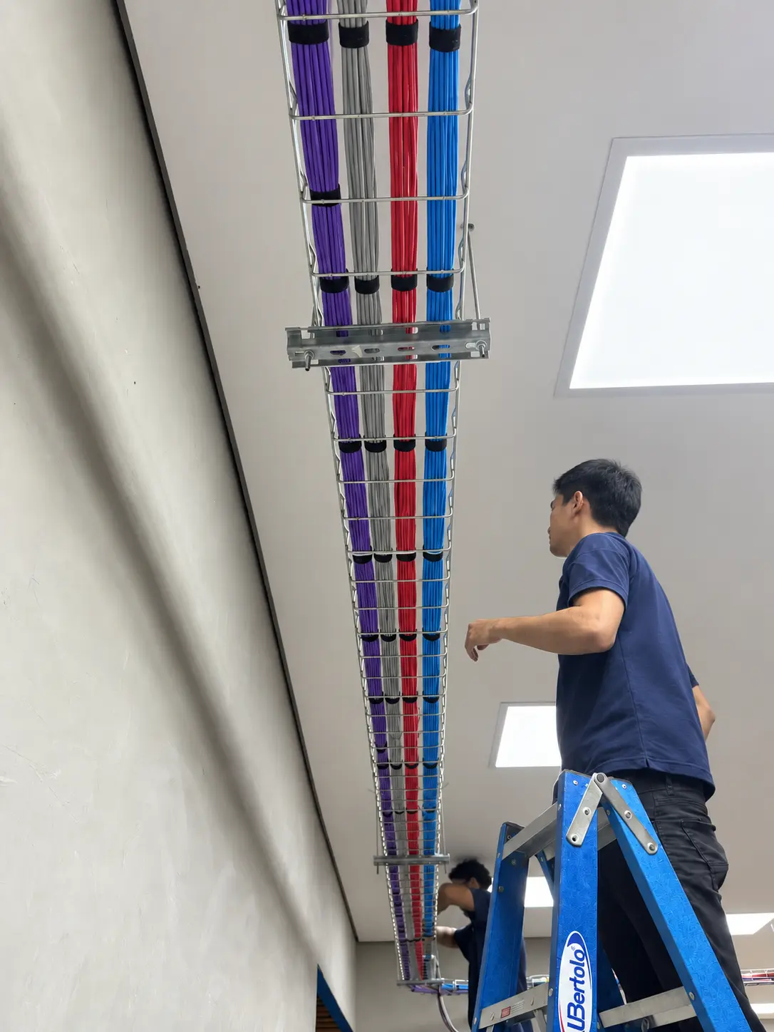 Equipe Skills Telecom em escadas trabalhando junto à eletrocalha com feixes de cabos organizados